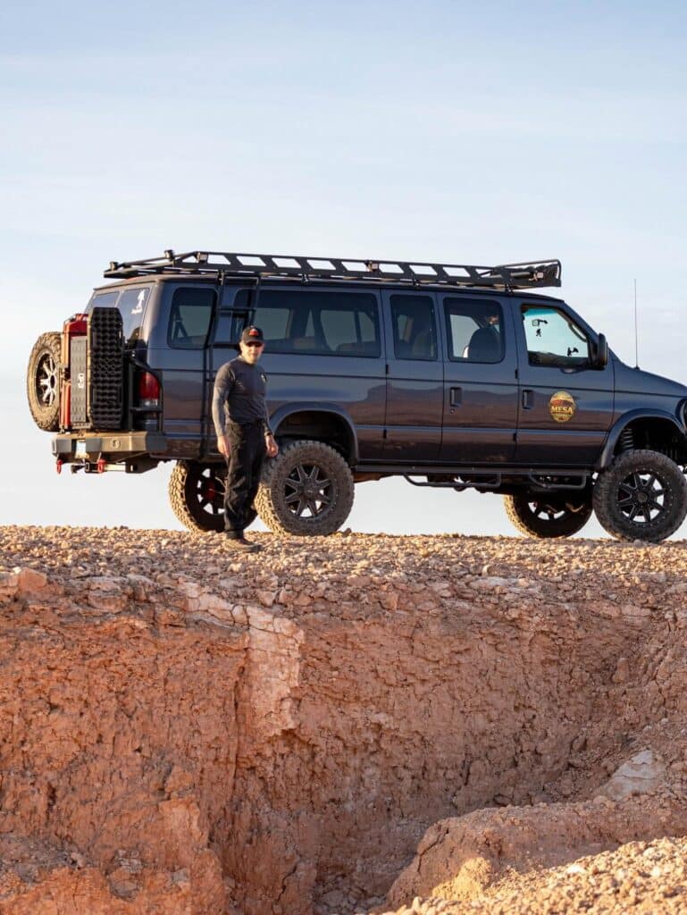 JB walking beside the Mesquite Mesa Tours van on the mesa edge at golden hour